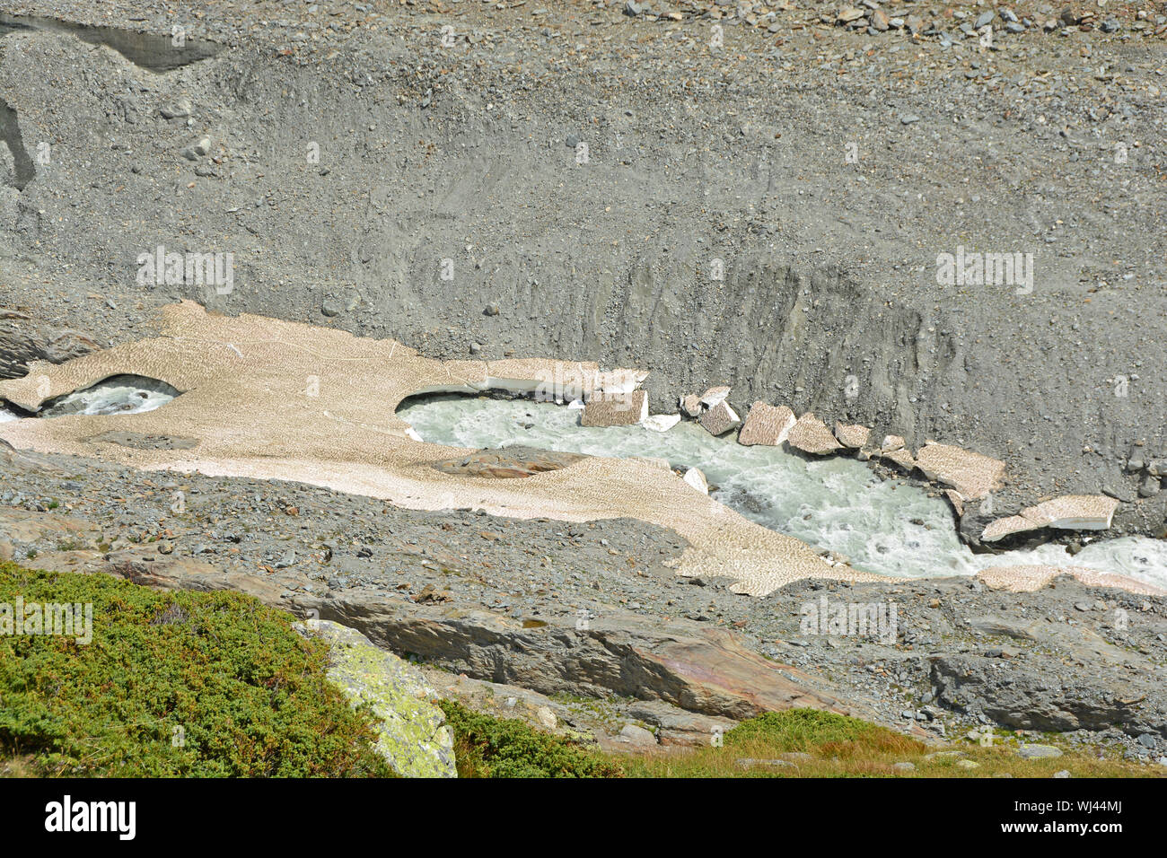 A glacier stream cuts through old snow bridges in the mountains. Top left parts of the glacier can be seen Stock Photo