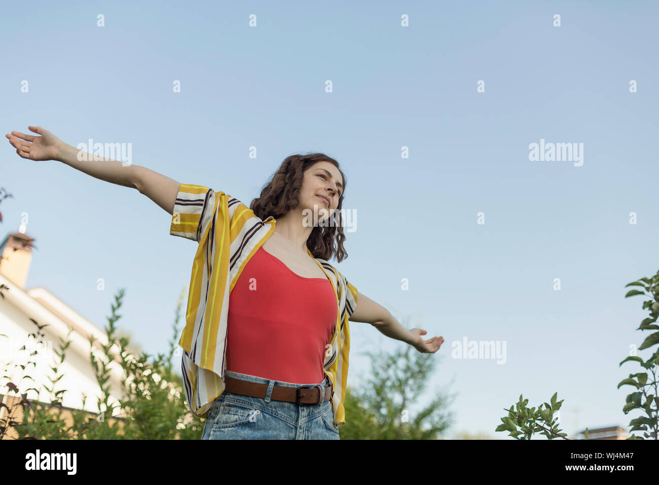 Carefree woman with arms outstretched in back yard Stock Photo
