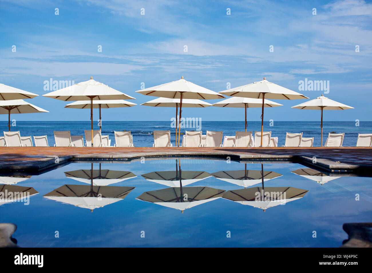 White beach umbrellas and lounge chairs at sunny ocean poolside, Punta de Mita, Nayarit, Mexico Stock Photo