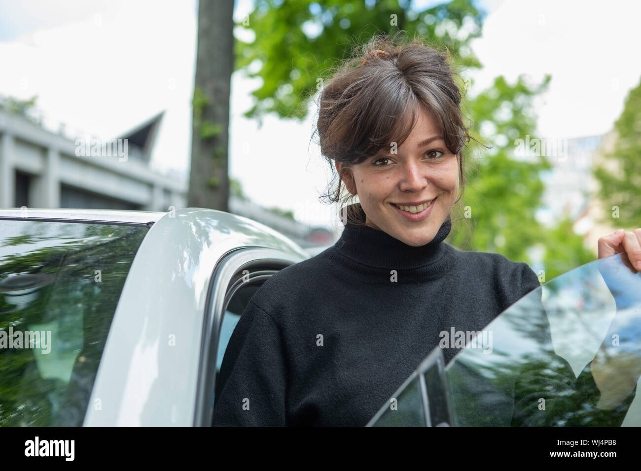 Portrait smiling young woman standing at car door Stock Photo