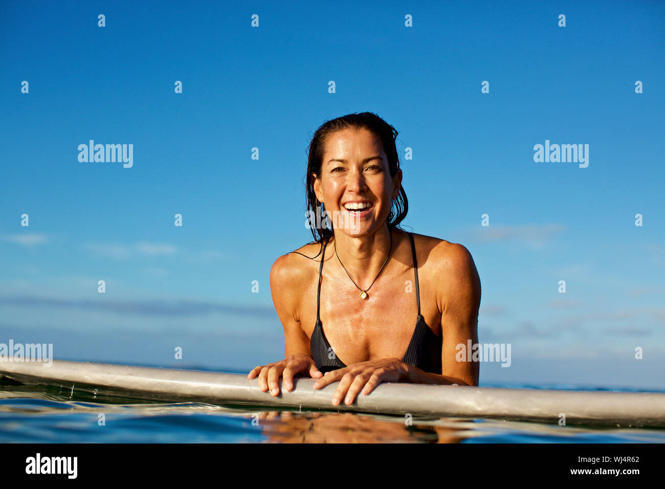 Portrait happy, confident female surfer leaning on surfboard in ocean Stock Photo