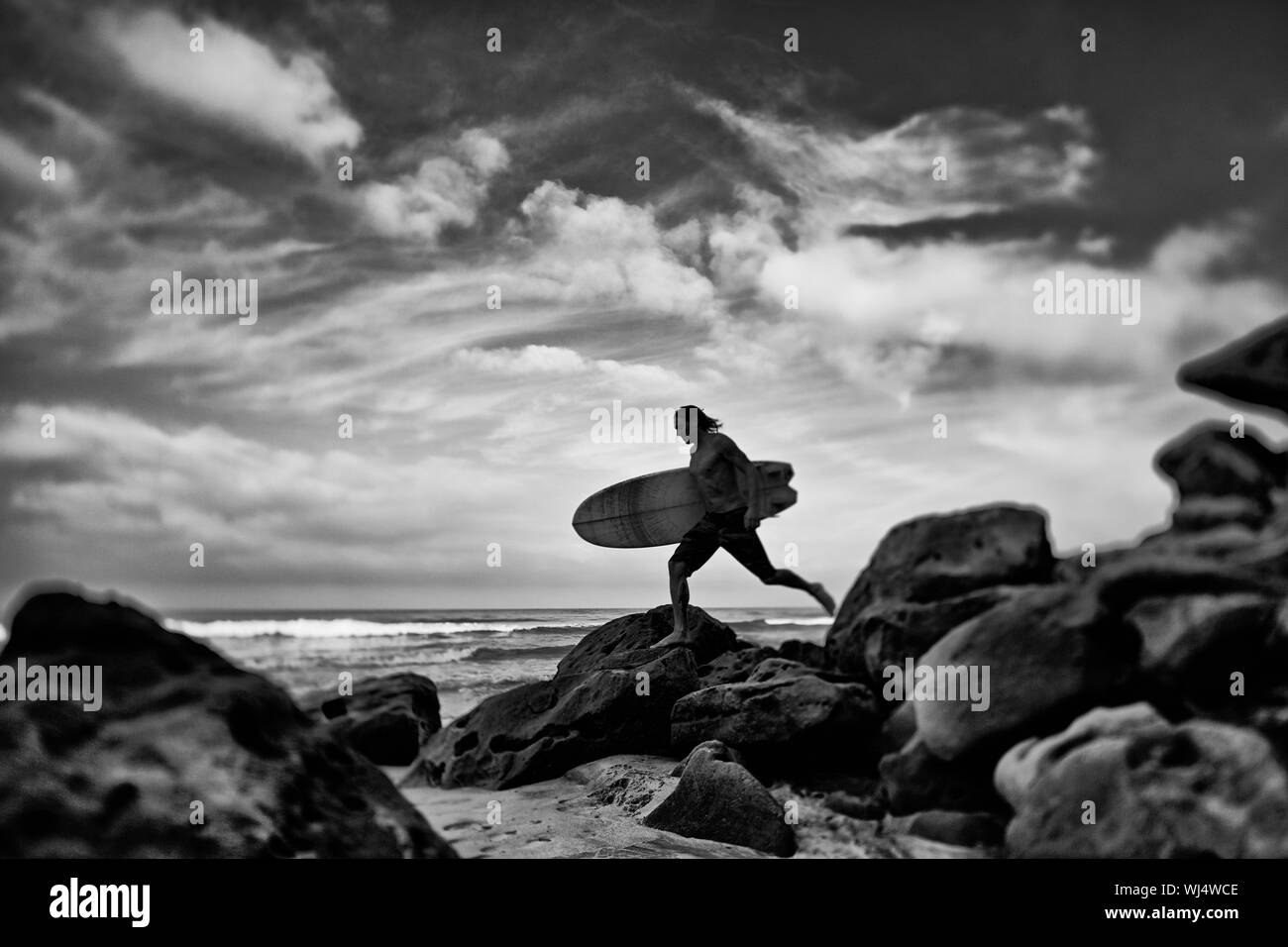 Male surfer with surfboard on rocky ocean beach, Higuera Blanca, Nayarit, Mexico Stock Photo