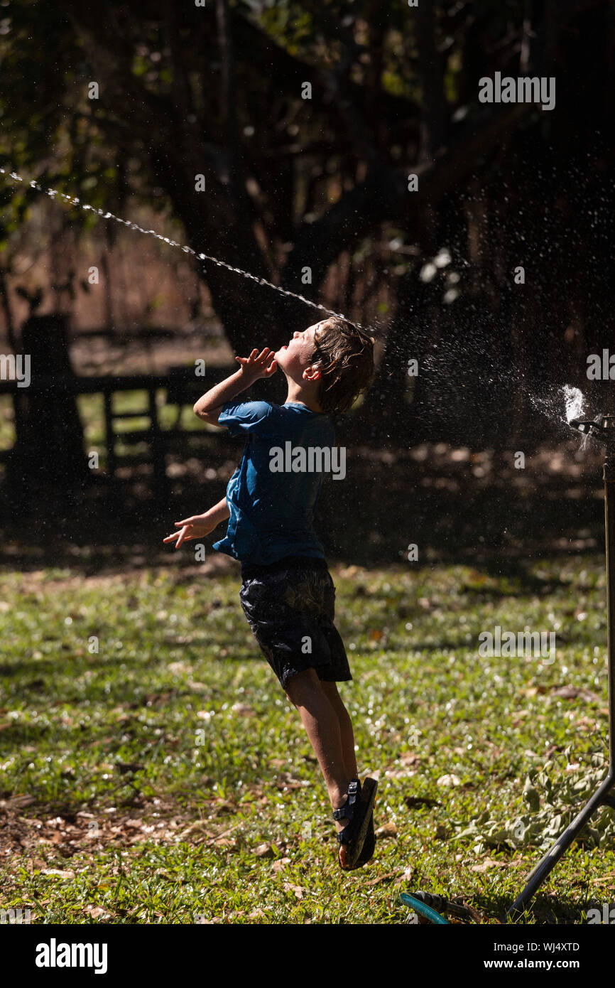 Carefree boy jumping up into sprinkler in sunny back yard Stock Photo
