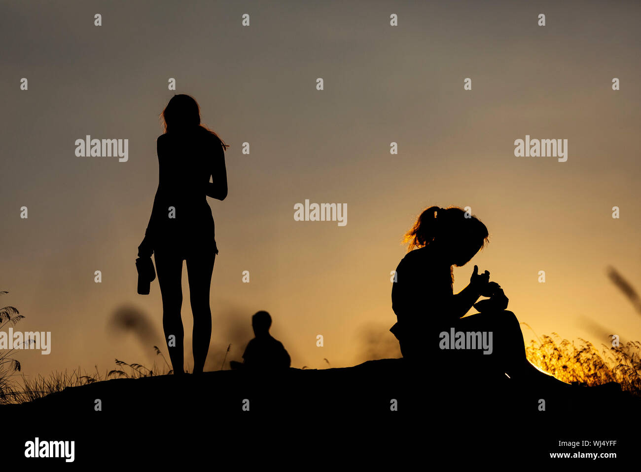 Silhouette women eating and drinking on hill at sunset Stock Photo