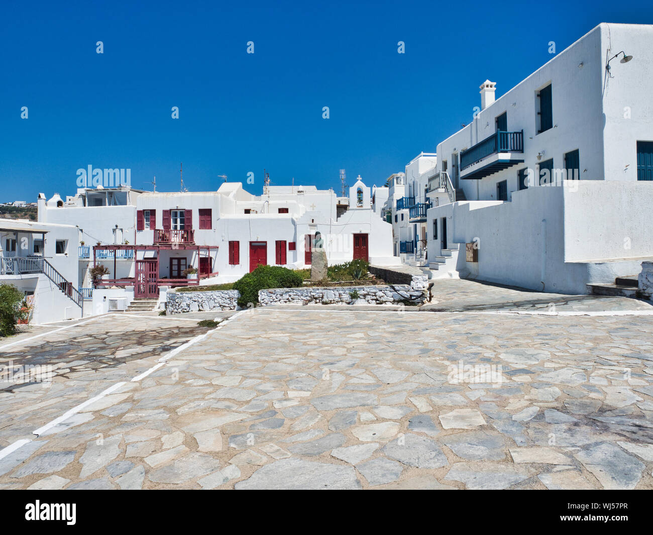 Ancient stone square surrounded by white houses against cloudless blue sky in town on Mykonos Island in Greece Stock Photo