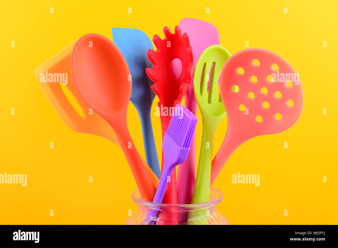 bright multi colored kitchen utensils on yellow background Stock Photo