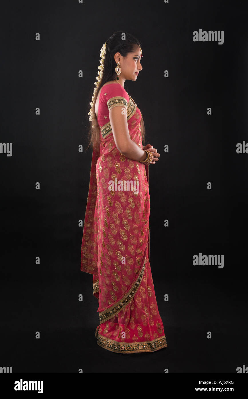 Full body side view or profile of traditional young Indian girl in sari costume standing isolated on black background. Stock Photo