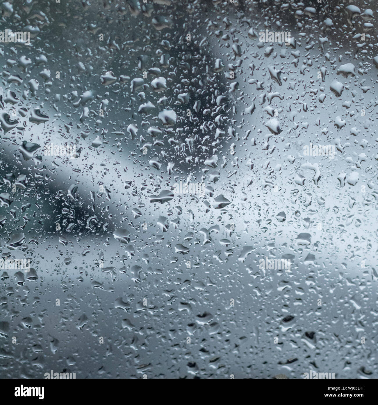 Raindrops on window glass with out of focus car in the background. Rain drops abstract, abstract water drops. Glass with water drops on it. Stock Photo