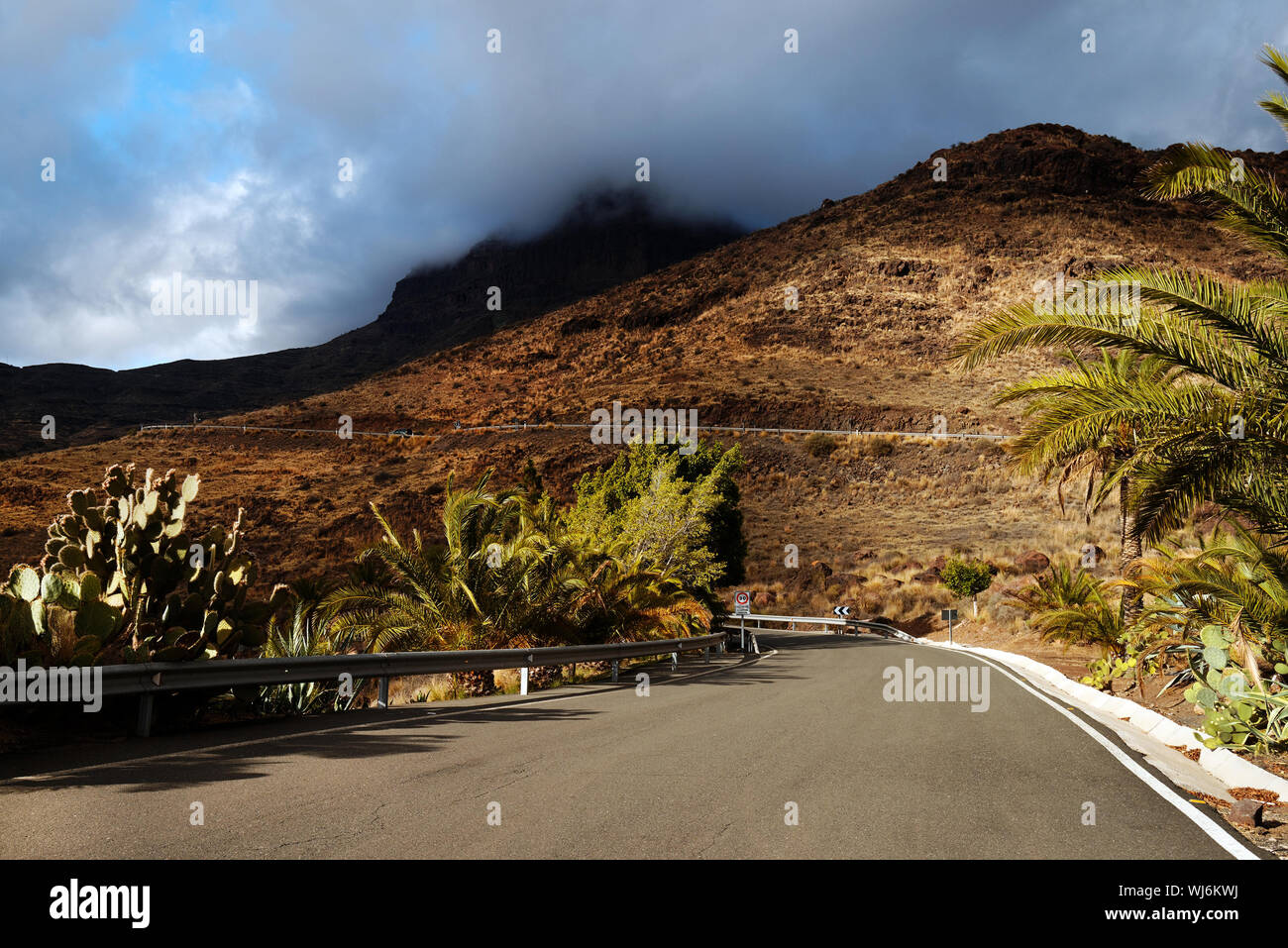 Diminishing Perspective Of Road Passing Through Mountains Against Cloudy Sky Stock Photo