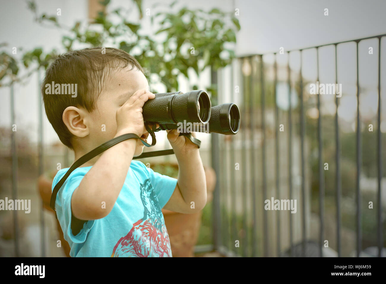 Little boy looking into vintage binoculars on a balcony. Stock Photo