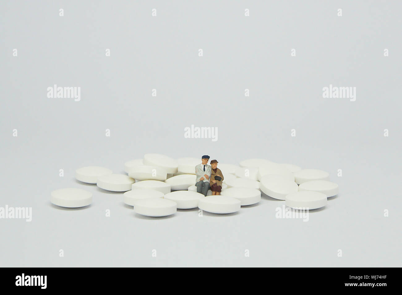 Elderly couple figure sitting on a pile of white pills. Stock Photo