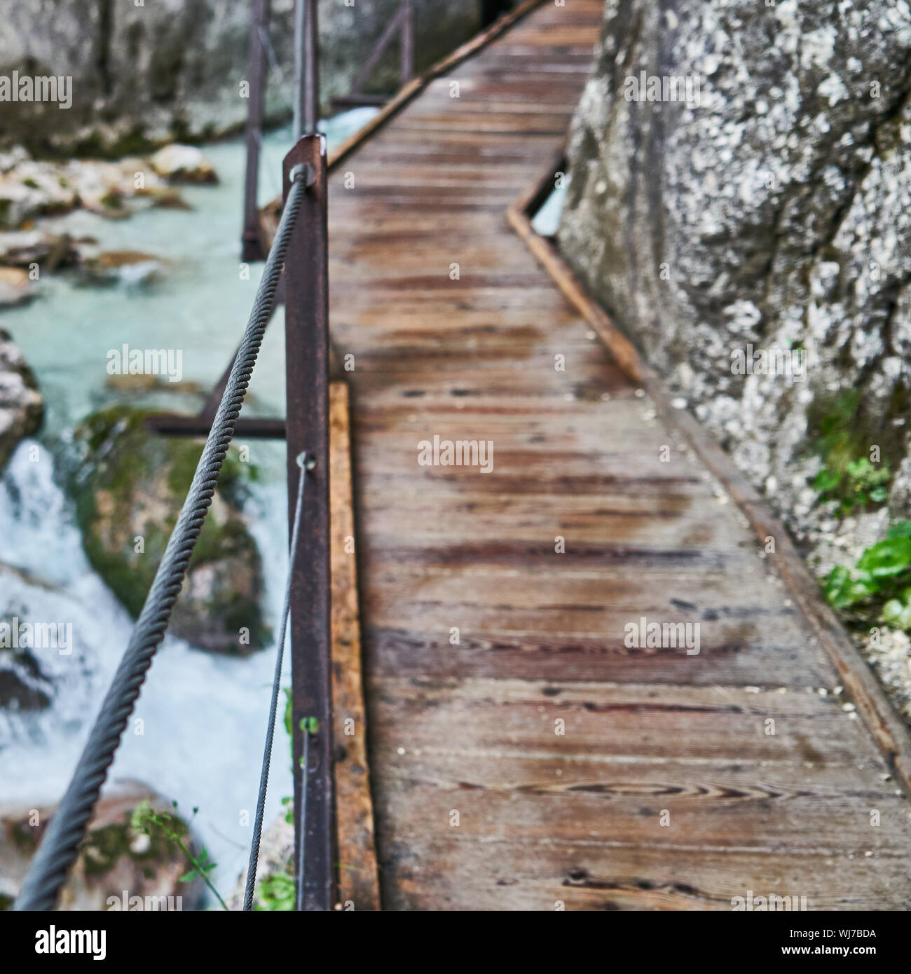 Narrow wobbly path over the Höllentalklamm gorge near Garmisch-Partenkirchen, selective focus on the steel cable, background deliberately blurred Stock Photo