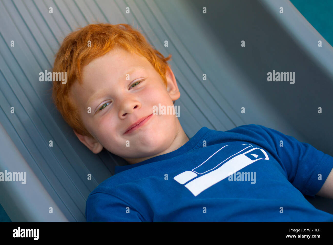 Boy lying on the floor. Portrait European boy with green eyes, looking directly at the camera. Overhead view. Funny little child with curly ginger Stock Photo