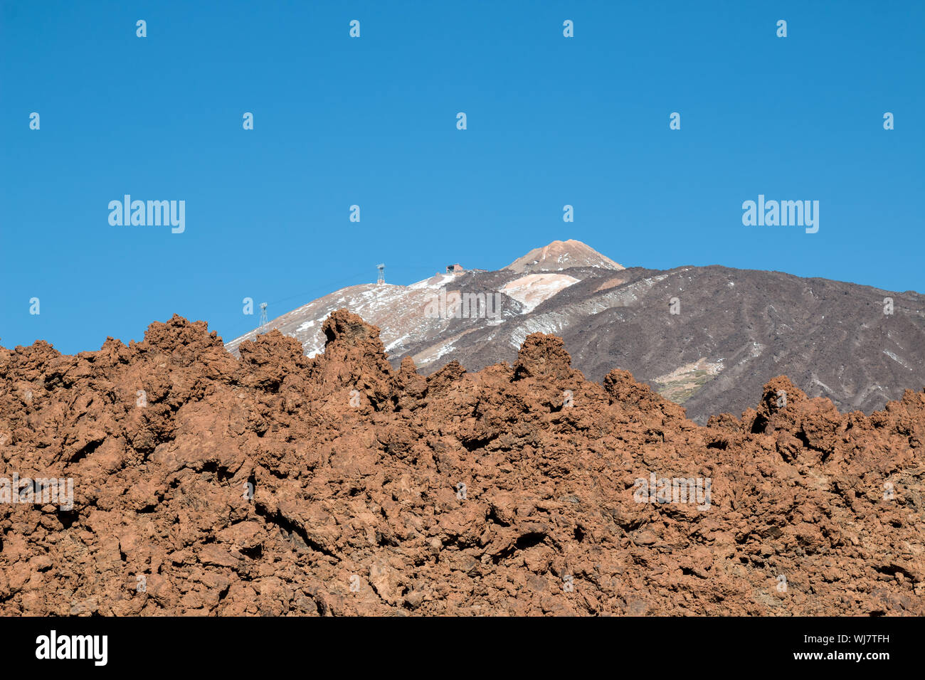 Light brown color of a wall made of sharp lava stones. In the background mountain and the peak of Pico del Teide. Bright blue sky. Tenerife, Canary Is Stock Photo