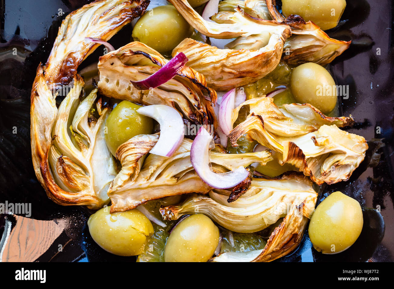 french cuisine - top view of baked pieces of fennel stalk with olives and red onion and dressing of orange, lemon juice and olive oil on black plate c Stock Photo