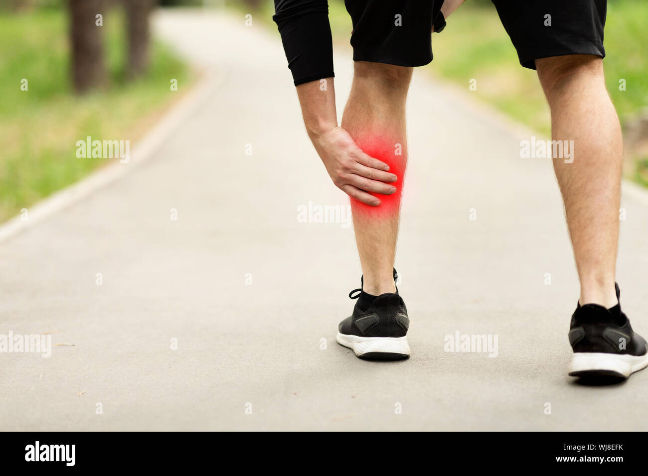 Man massaging painful calf muscle with red sore spot outdoors Stock Photo