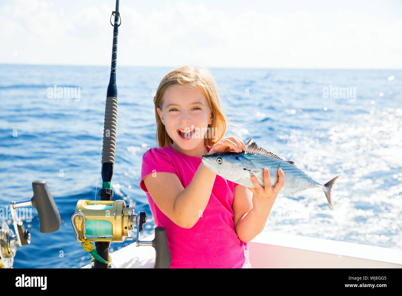 Blond kid girl fishing tuna bonito sarda fish happy with trolling catch on boat deck Stock Photo