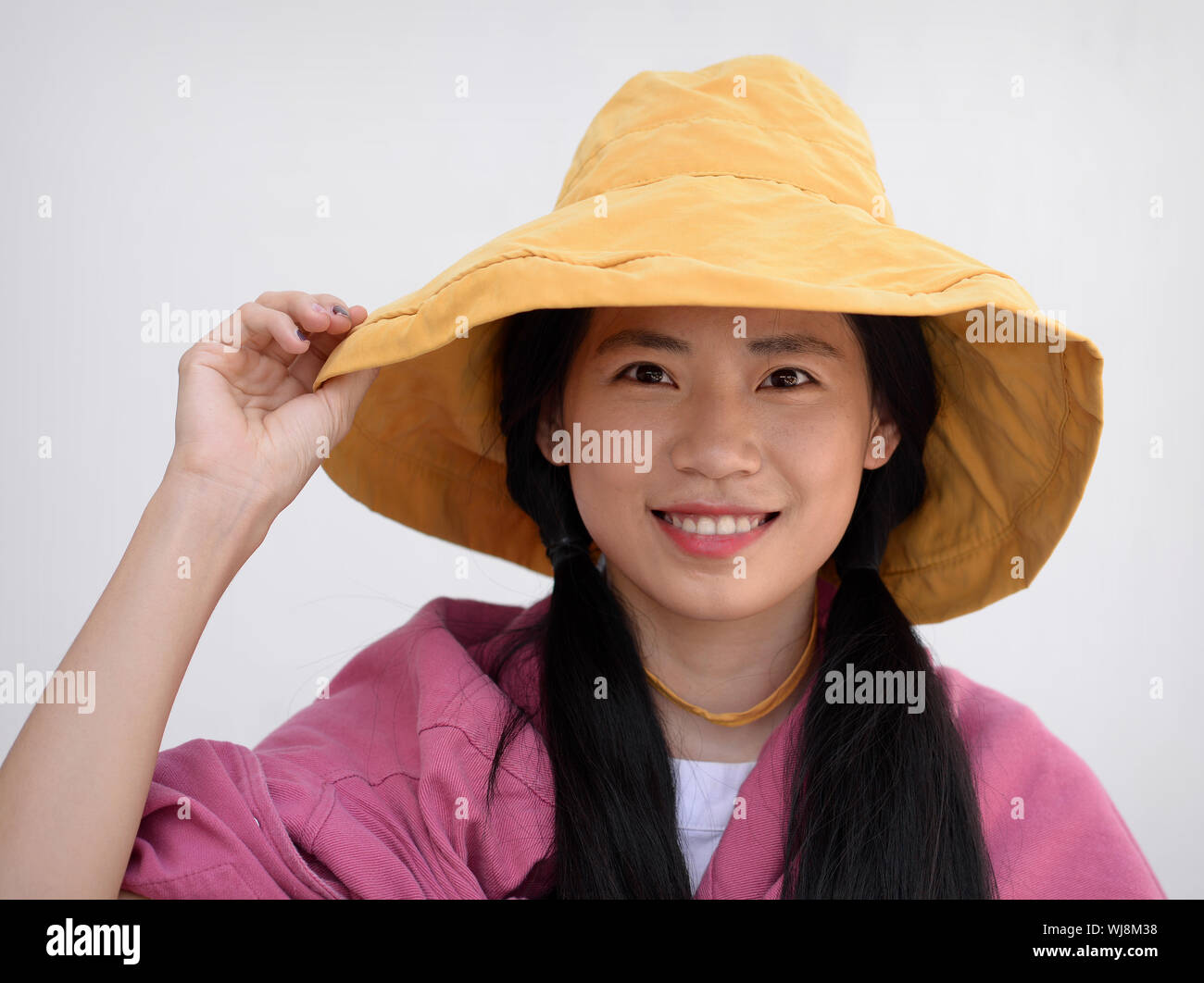 Pretty Thai girl with a yellow floppy hat smiles for the camera. Stock Photo