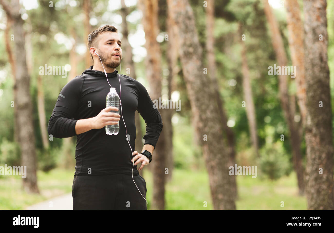 Man resting and drinking water after jogging in park Stock Photo
