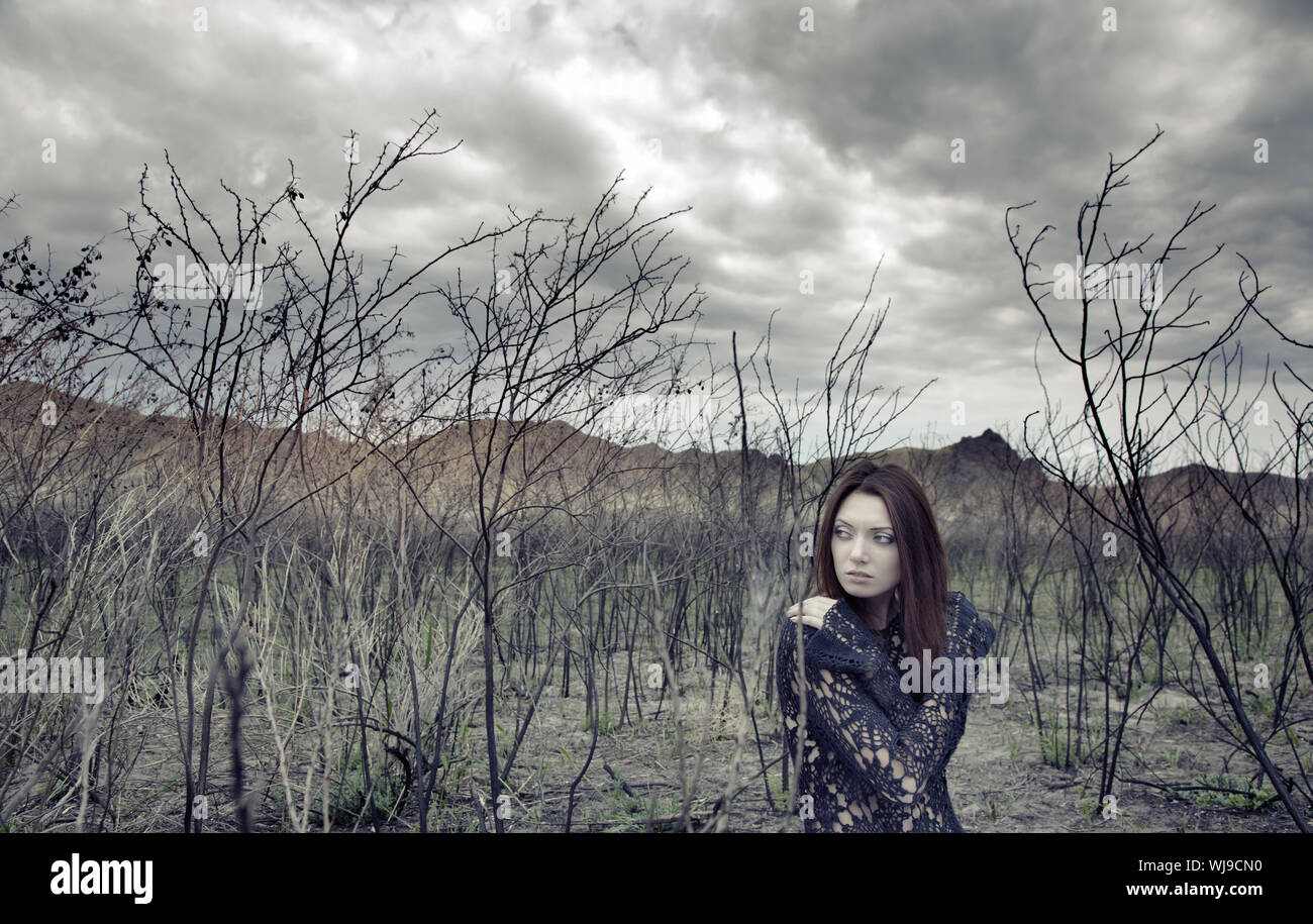 Sad alone woman in the dead bushes and thunderous sky on a background. Artistic colors added for movie effect Stock Photo