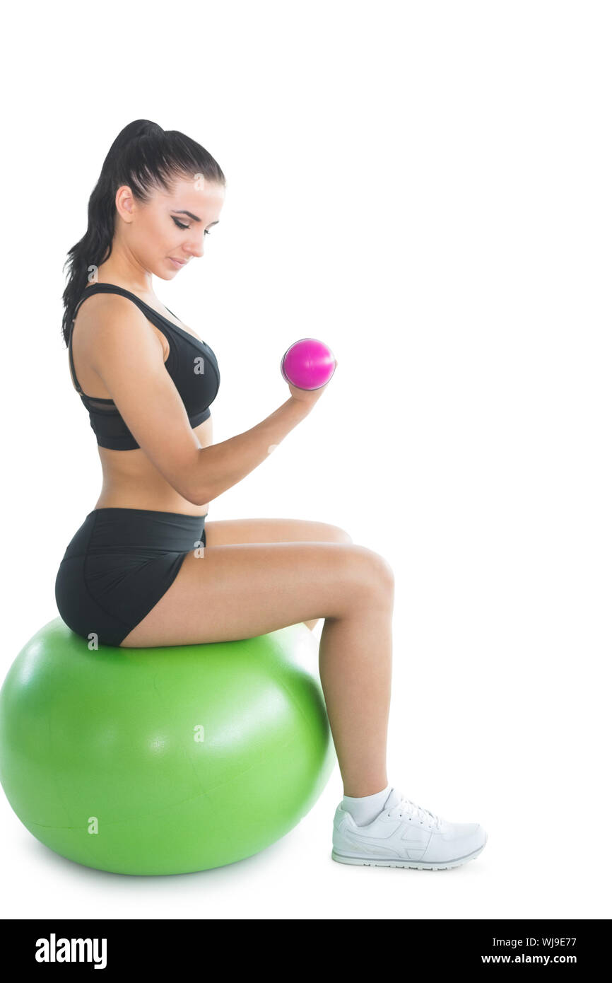 Attractive young woman sitting on an exercise ball using pink dumbbells