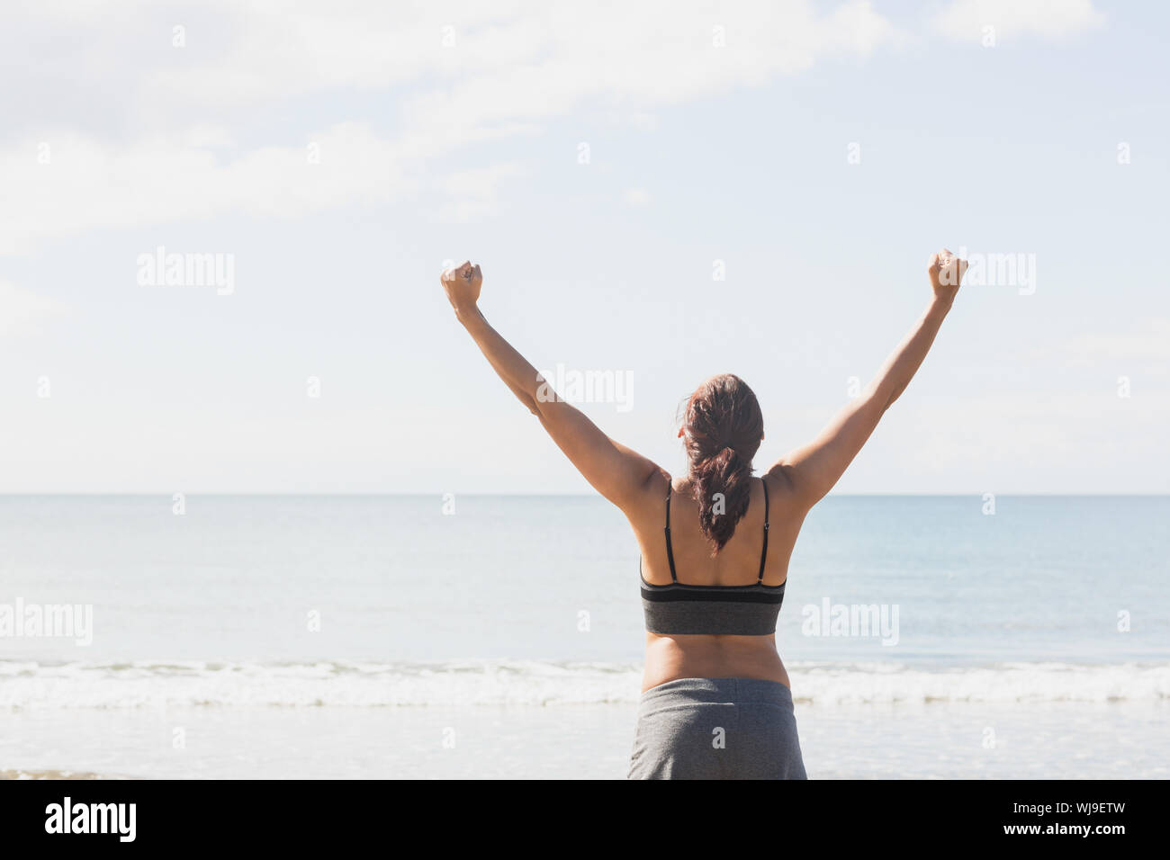Content brunette woman standing on the beach raising her arms Stock ...