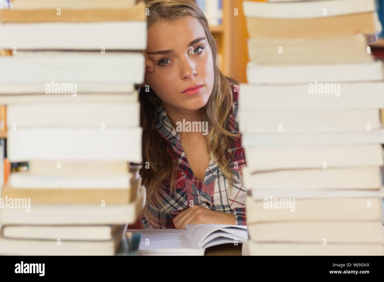 Stern pretty student studying between piles of books in library Stock ...