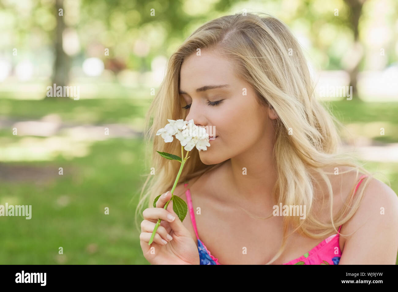 Side view of cute casual woman smelling a white flower with closed eyes ...