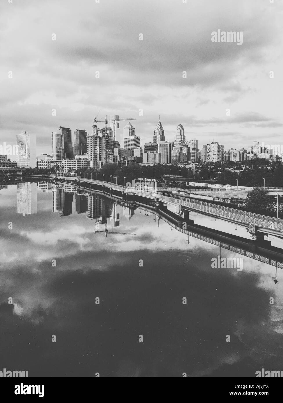 Reflection Of Bridge And Buildings On Schuylkill River Against Cloudy Sky Stock Photo