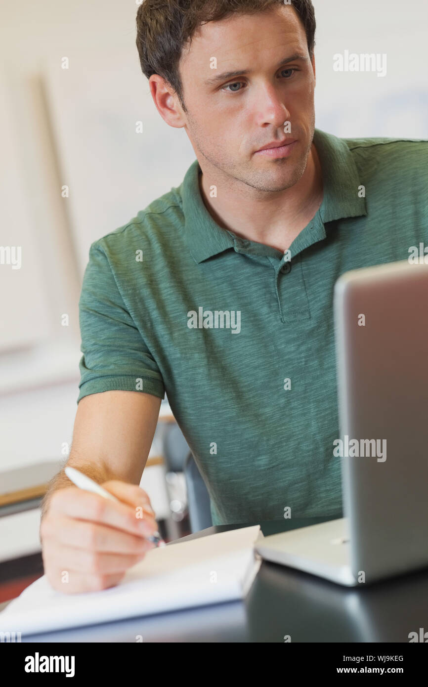 Focused handsome mature student using his notebook for learning while sitting in classroom Stock Photo