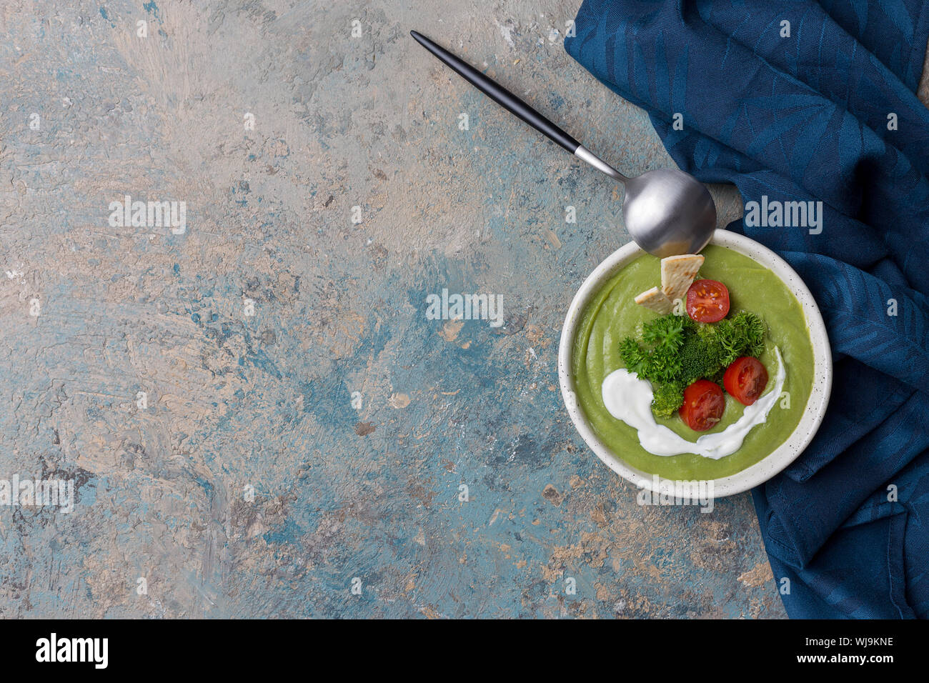Table set with cream soup with broccoli, spoon and blue napkin on concrete background. Harvest food, top view, flat lay Stock Photo