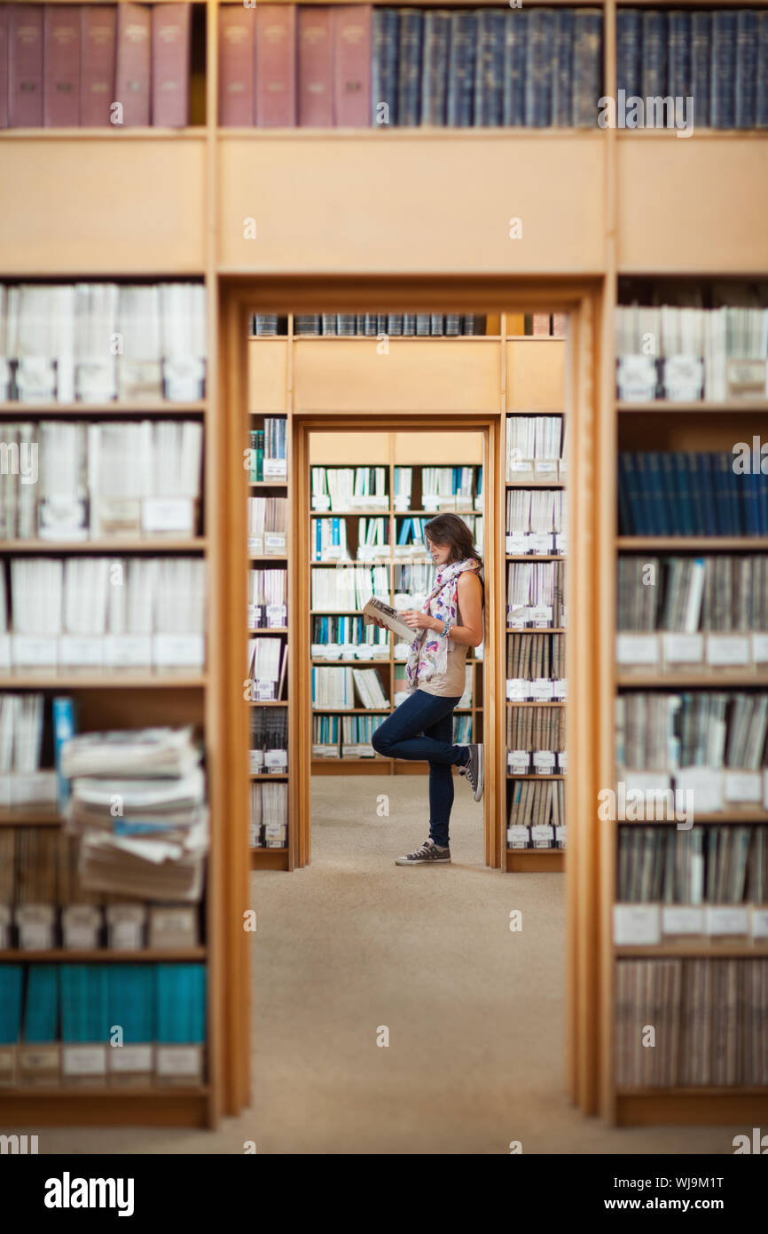 Full length side view of a female student reading a book in the library ...