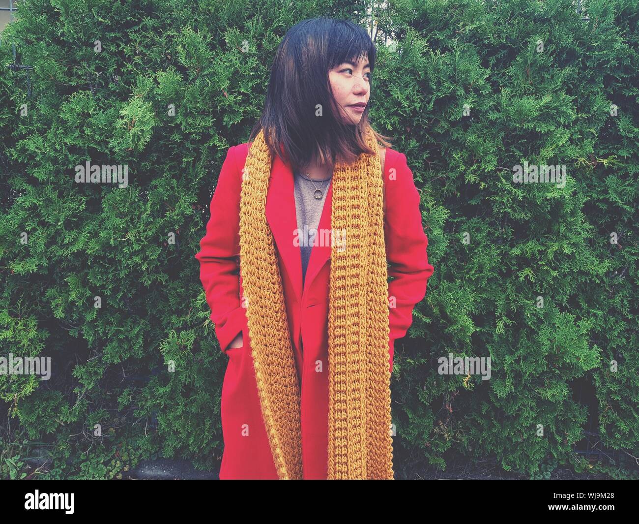 Woman Wearing Red Overcoat While Standing By Plants Stock Photo