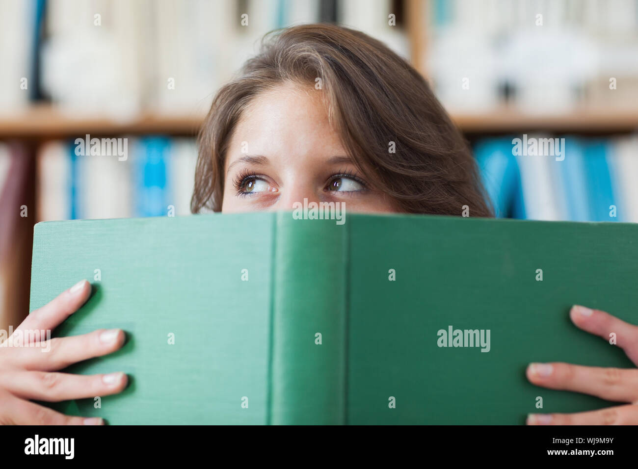 Close-up portrait of a female student holding book in front of her face ...