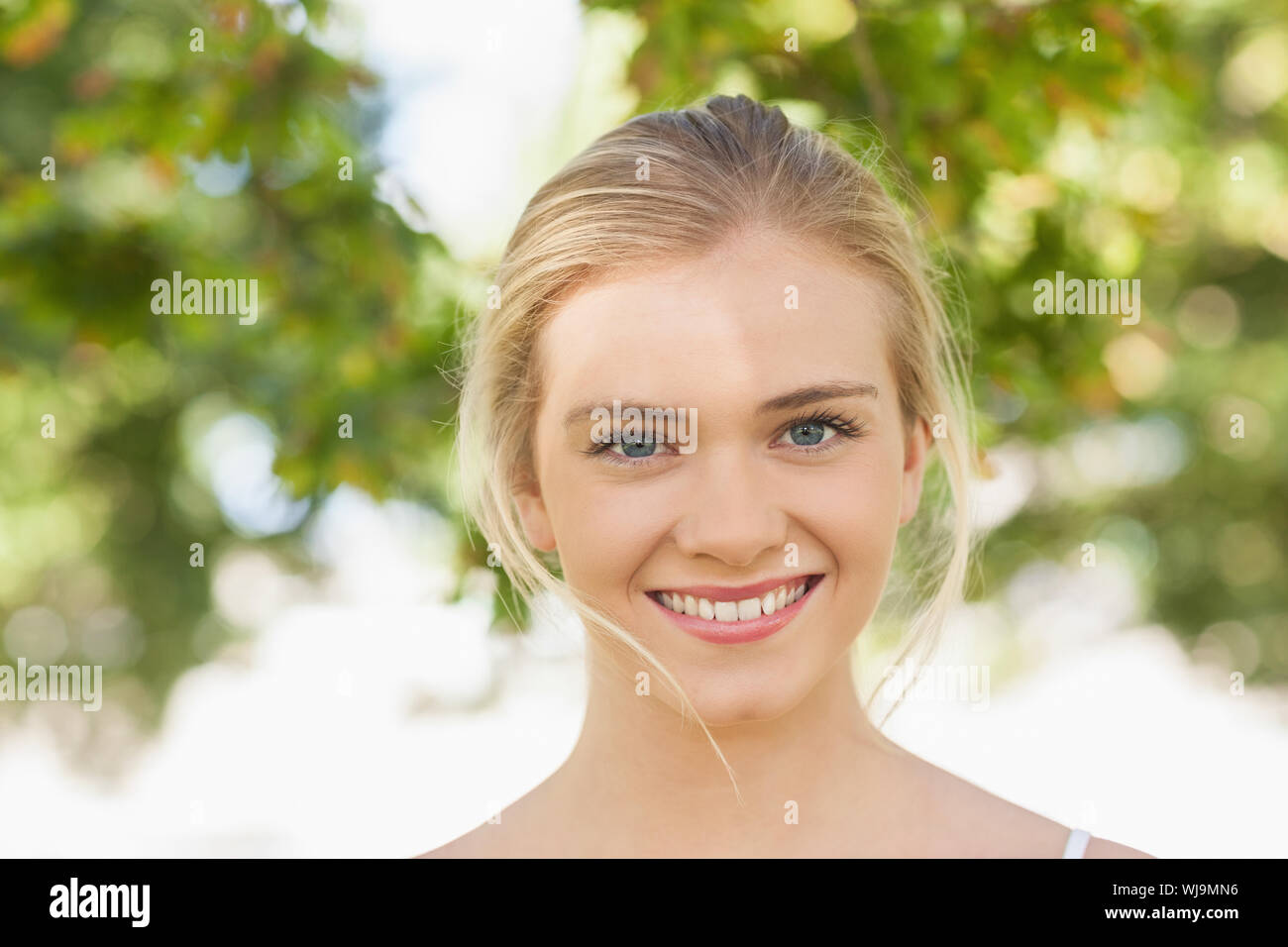 Beautiful young woman posing in a park smiling at camera Stock Photo ...