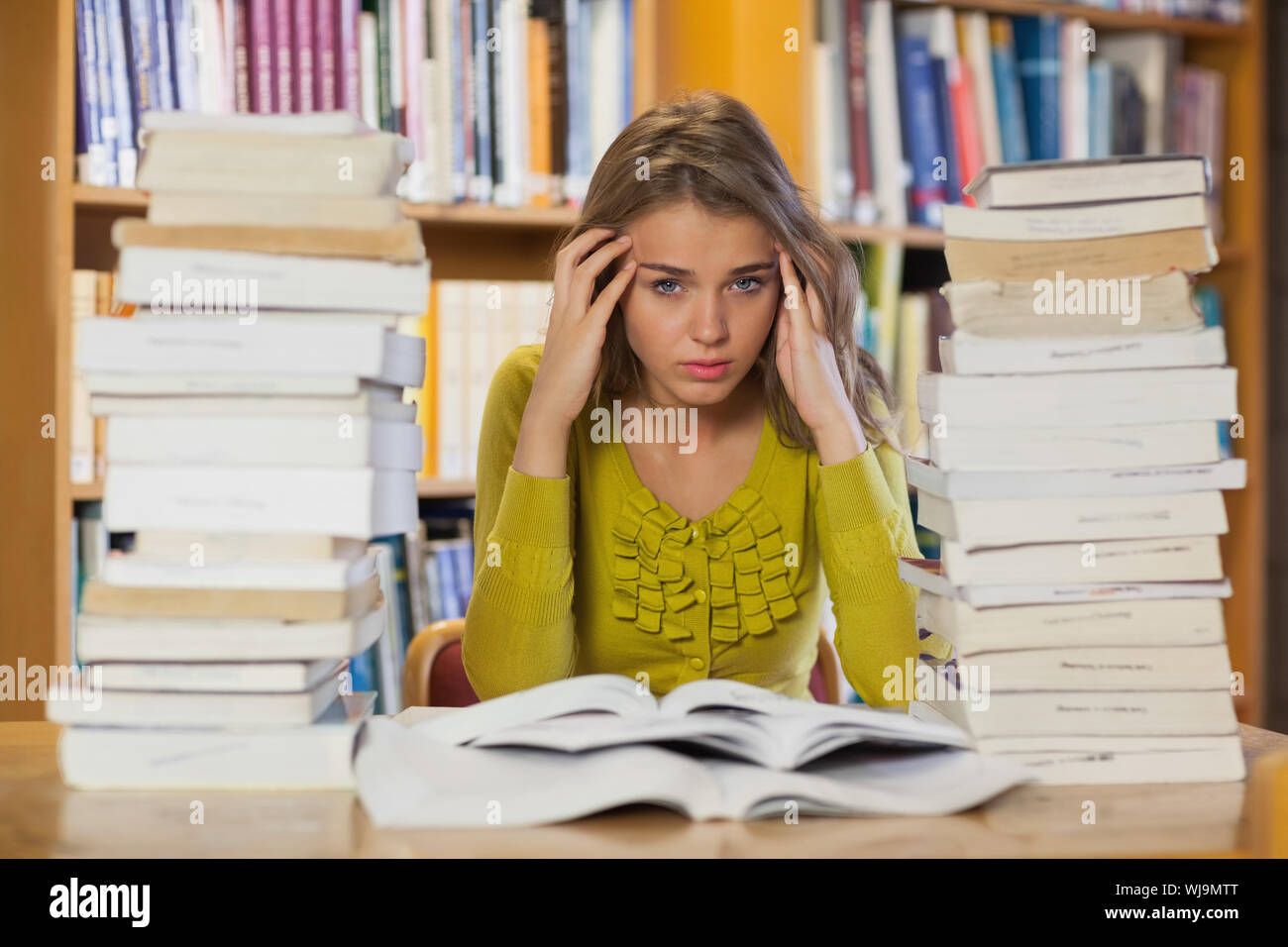 Tired pretty student studying between piles of books in library Stock ...