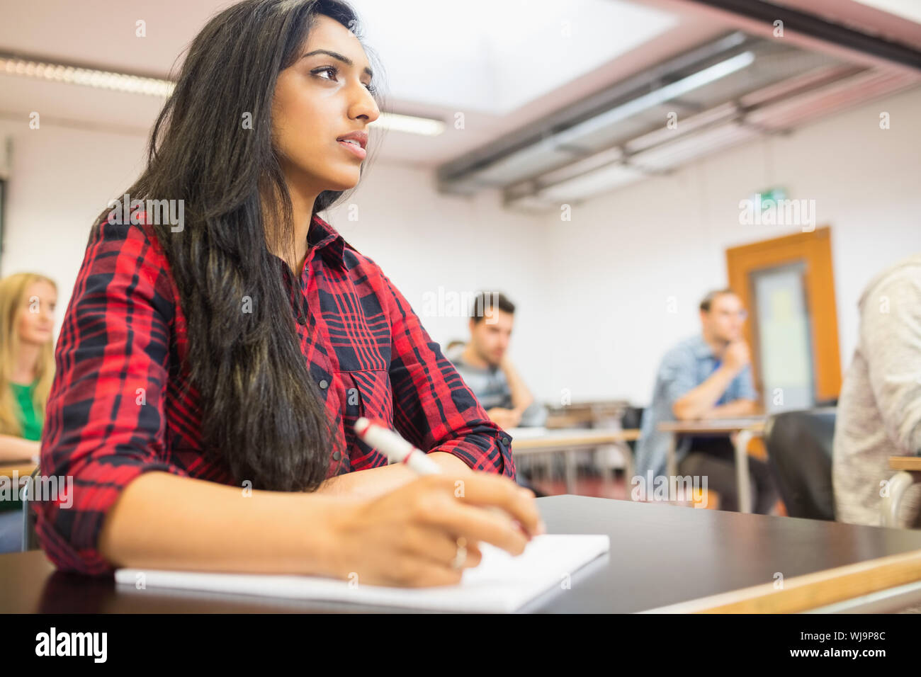 Young female student with others writing notes in the classroom Stock Photo