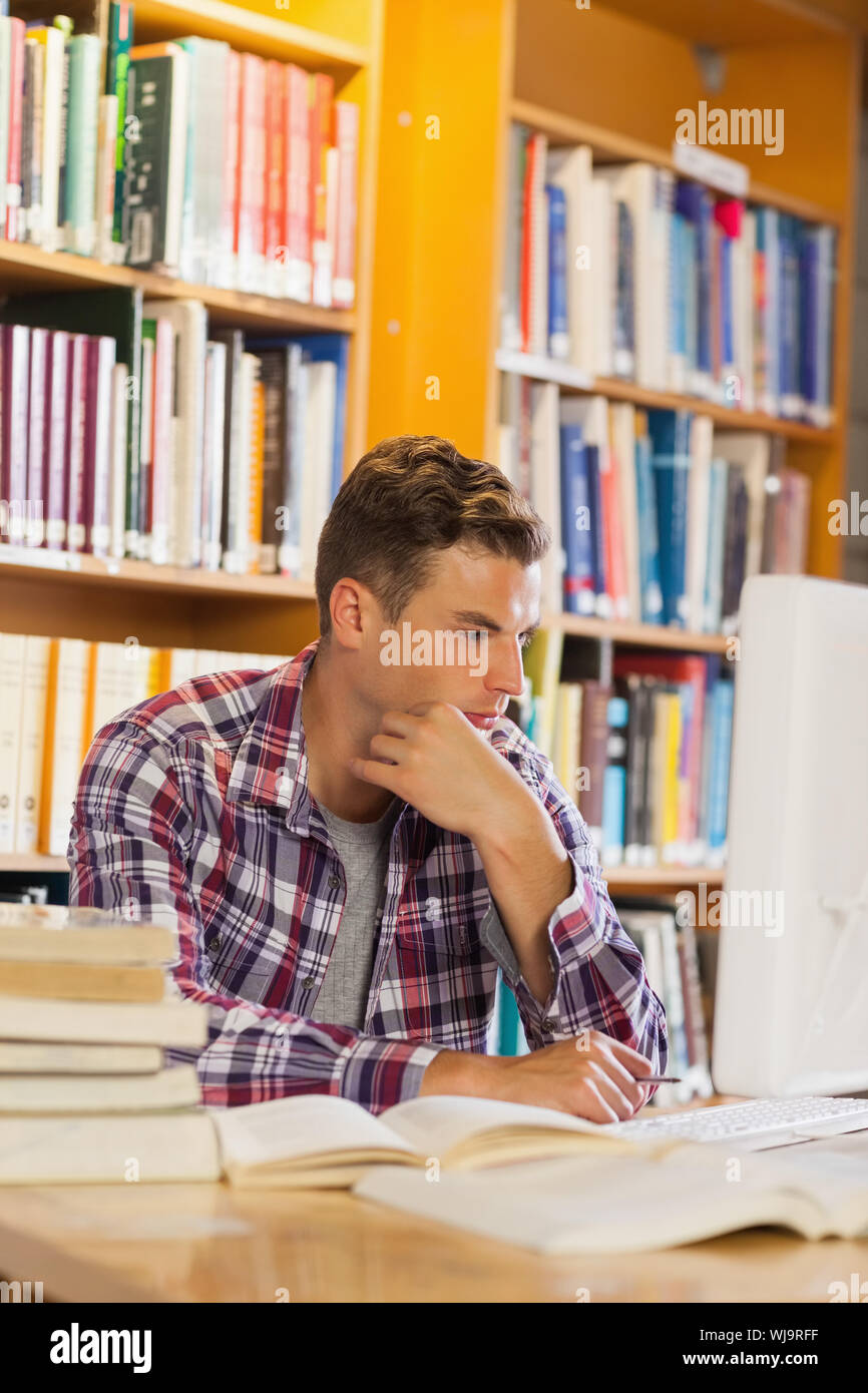 Handsome thoughtful student using computer in library Stock Photo