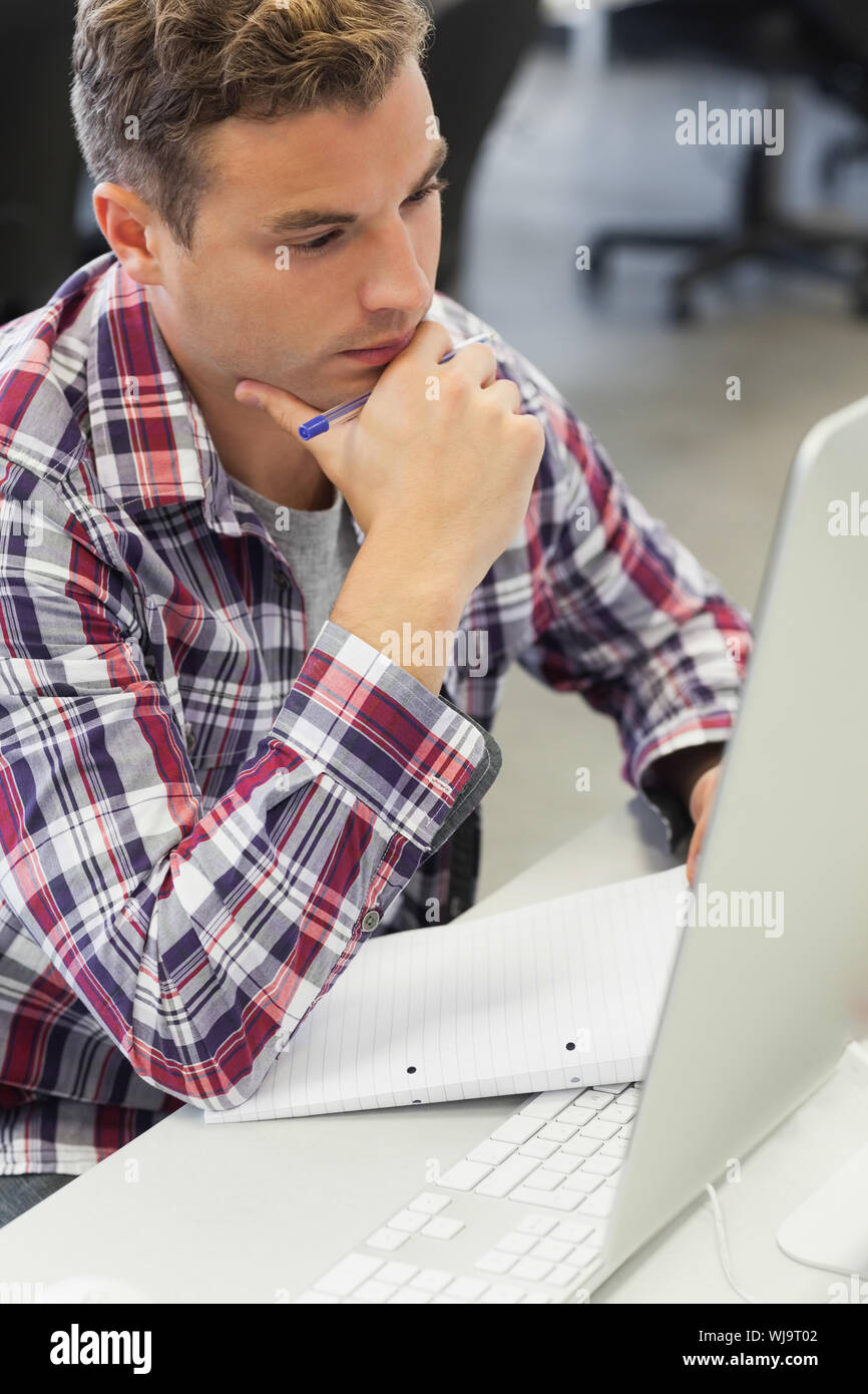 Handsome thoughtful student using computer taking notes in computer room at college Stock Photo