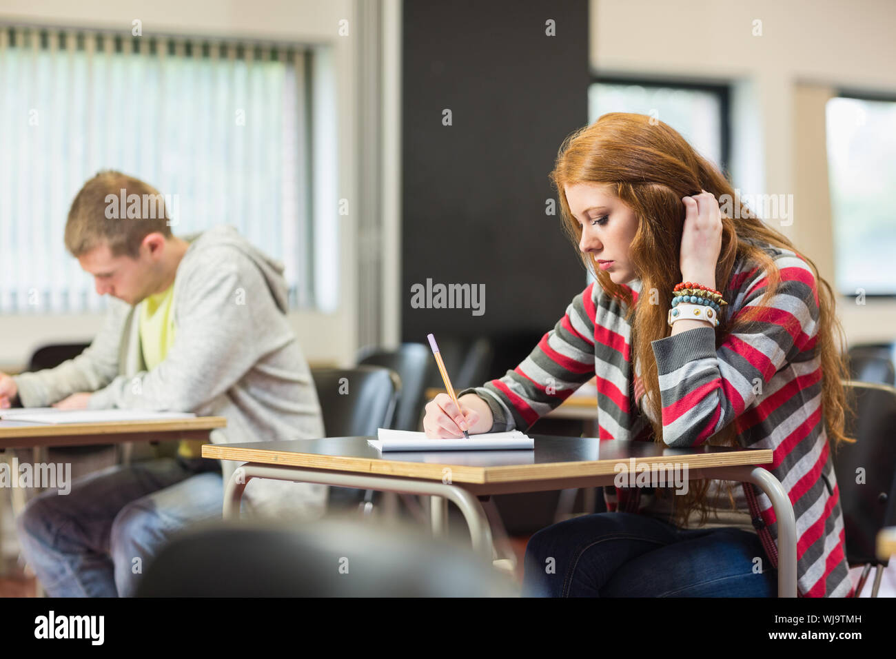 Young female student with others writing notes in the classroom Stock Photo
