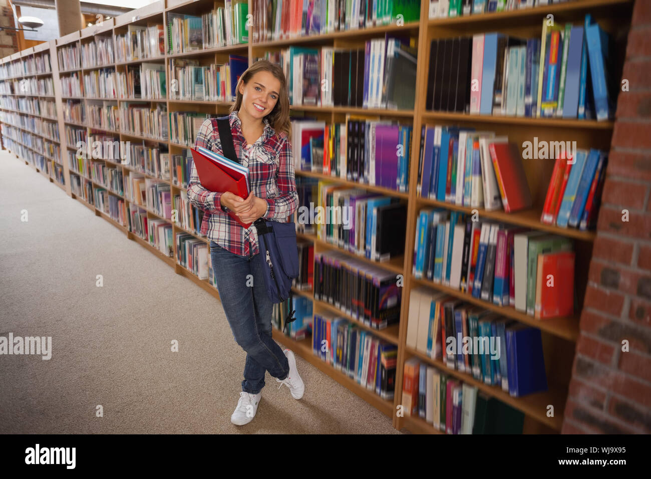 Pretty smiling student holding notebooks in library Stock Photo - Alamy