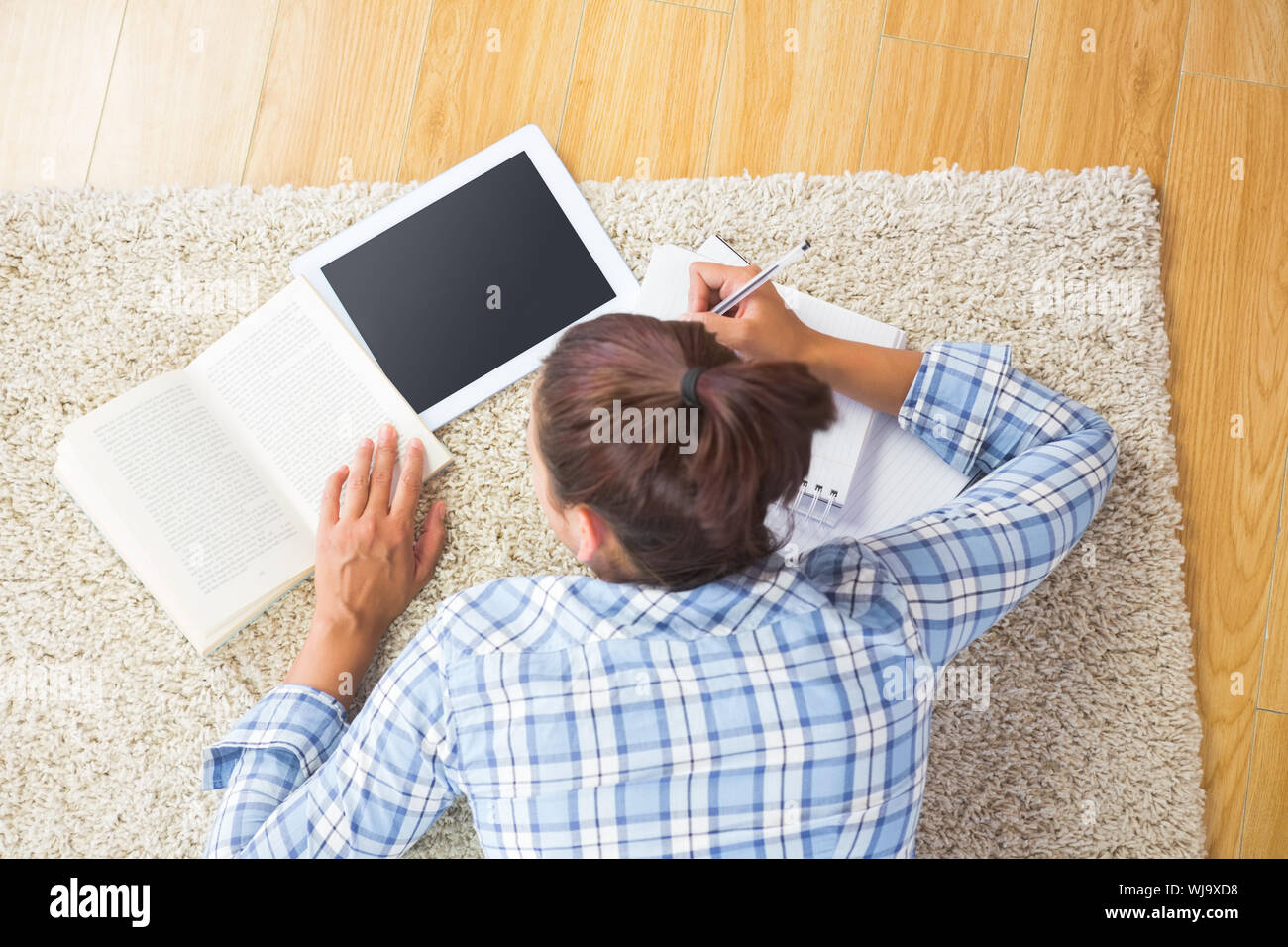 Brunette female student lying on the floor doing assignments using her ...