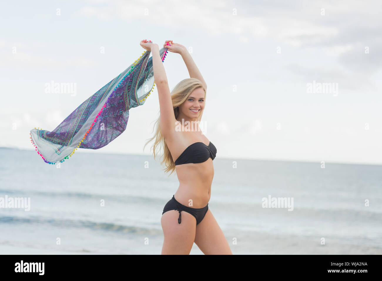 Side view of a happy young woman in bikini holding out scarf at the beach Stock Photo