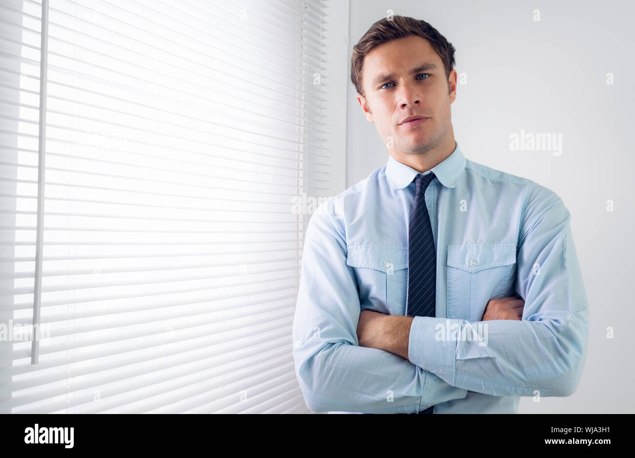Portrait of an elegant young businessman standing with arms crossed in ...