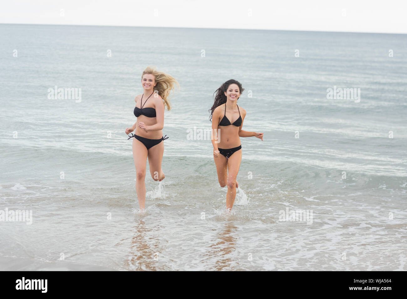 Portrait of two smiling young bikini women running in water at the beach Stock Photo