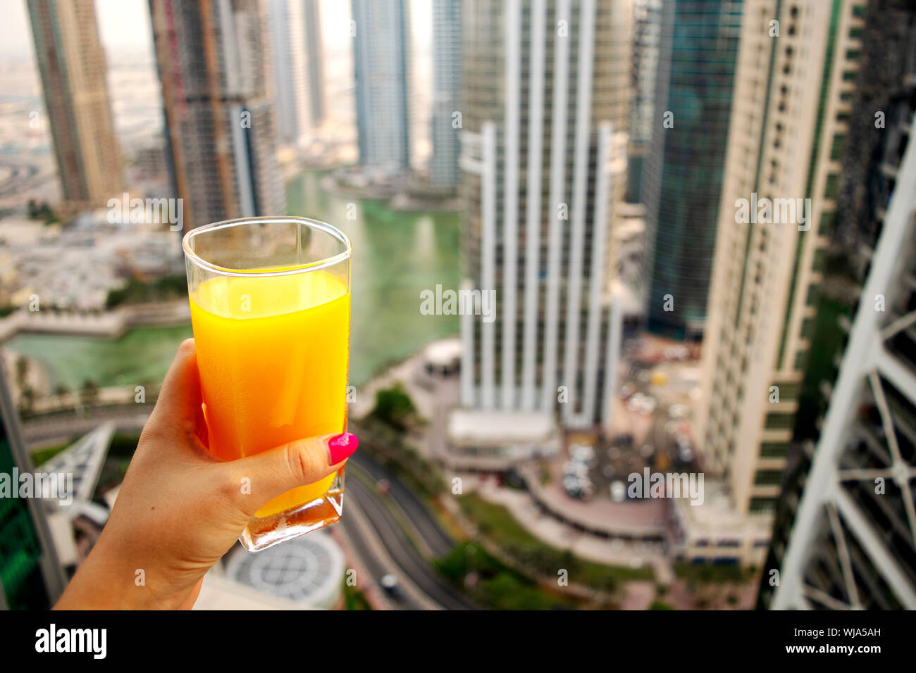 Female hand holds glass of fresh cold orange juice with city