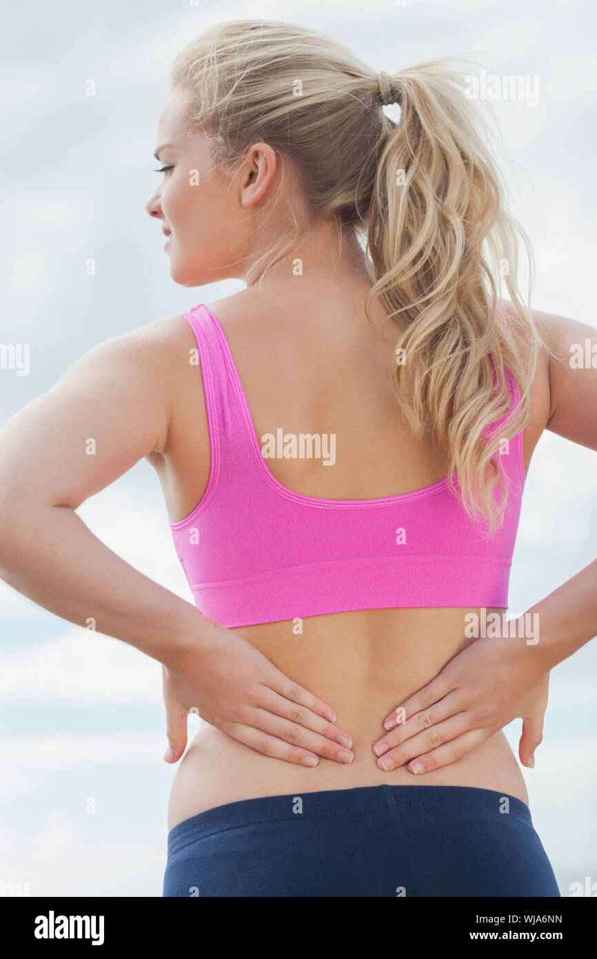 Rear view of a healthy woman in sports bra suffering from back