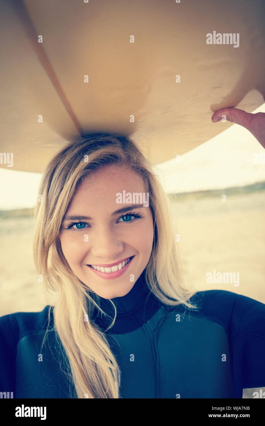 Portrait of a smiling young woman in wet suit holding surfboard over head at beach Stock Photo