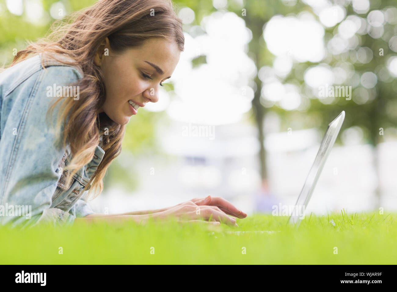 Happy student lying on the grass using her laptop Stock Photo