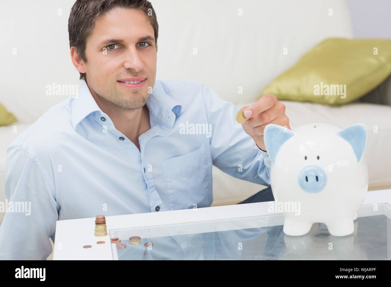 Casual man putting some coins into a piggy bank in living room Stock ...
